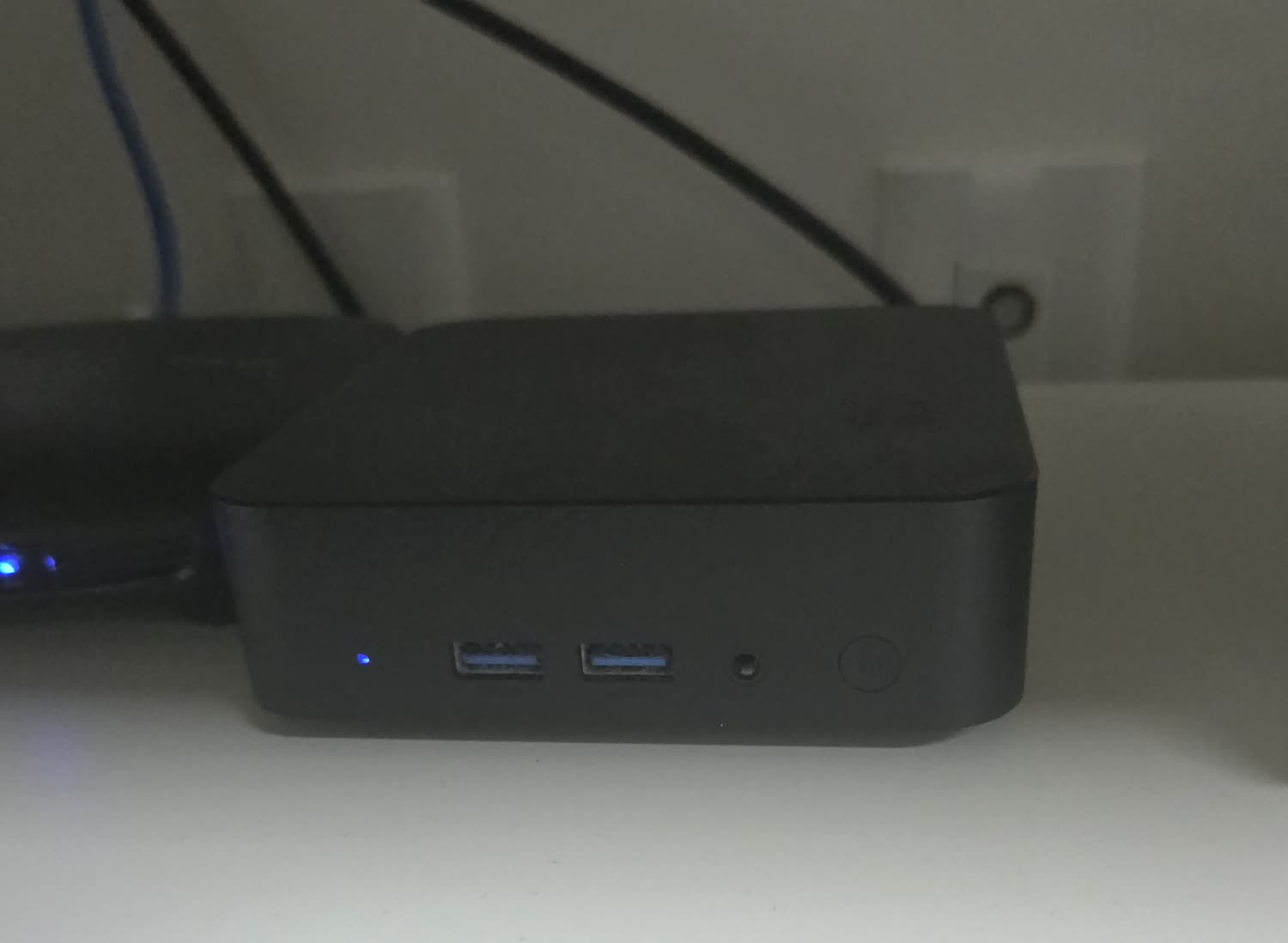 책상 위에 놓인 검은색 N100 미니PC. 앞면에 USB 포트 두 개와 전원 버튼이 있고 파란 전원 표시등이 켜져 있다.